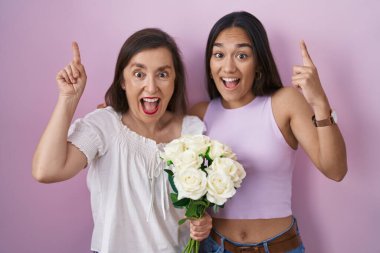 İspanyol anne ve kızı ellerinde bir buket beyaz çiçekle şaşkın ve şaşırmış bir şekilde parmaklarını kaldırıp kollarını kaldırdılar.. 