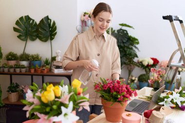Genç beyaz kadın çiçekçi çiçekçide dağıtıcı sulama bitkisi kullanıyor.