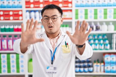 Eczanede çalışan Çinli genç adam avuçlarıyla jestleri durduruyor, kızgın ve hayal kırıklığına uğramış bir ifade sergiliyor. 