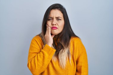 Tecrit edilmiş arka planda duran genç İspanyol kadın diş ağrısı ya da diş hastalığından dolayı acı dolu bir ifadeyle ağıza dokunuyor. dişçi 