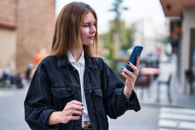 Sokakta ciddi yüzlü akıllı telefon kullanan genç sarışın kadın.