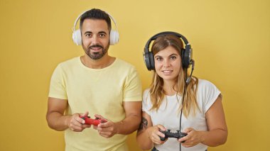 İzole edilmiş sarı arka planda gülümseyen erkek ve kadın video oyunu oynuyorlar