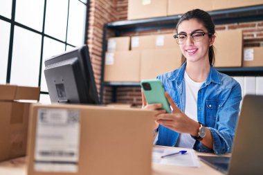 Genç, güzel, İspanyol bir kadın. İş kadını. Ofiste dizüstü bilgisayar ve akıllı telefon kullanıyor.