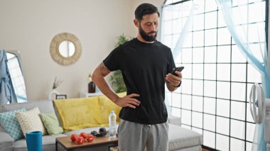 Genç İspanyol adam evde akıllı telefon kullanıyor.