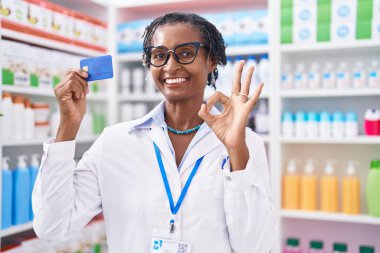 Eczanede çalışan Afrikalı bir kadın elinde kredi kartıyla çalışıyor. Parmaklarıyla imza atıyor, gülümsüyor. 