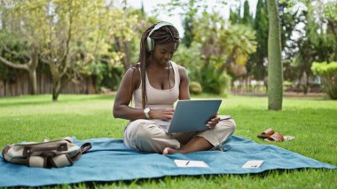 Kampüs üniversitesinde bilgisayar ve kulaklık kullanan Afrikalı Amerikalı bir kız öğrenci.