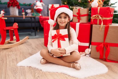 Sevimli İspanyol kız Noel hediyesini kucaklıyor. Evde yerde oturuyor.