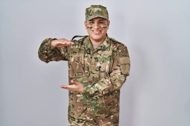 İspanyol genç adam kamuflaj üniforması giyiyor. Ellerinde büyük ve büyük bir işaret var. Ölçü sembolü. Kameraya bakıp gülümsüyor. ölçüm kavramı. 