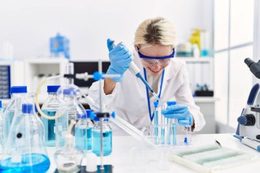 Laboratuvarda test tüpüne sıvı döken genç sarışın bilim kadını.