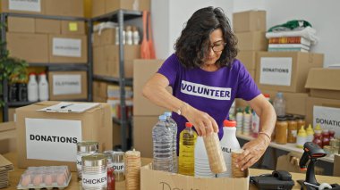 Orta yaşlı İspanyol bir kadın yardım merkezinde bağışlamak için karton kutuya ürünler koyuyor.