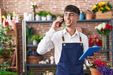 Çiçekçide dokunmatik ped kullanarak akıllı telefondan konuşan İspanyol bir çiçekçi.