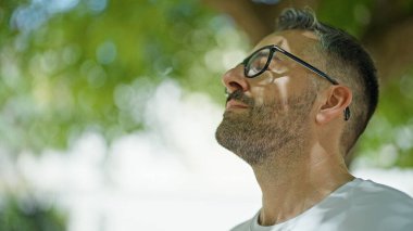 Parkta gözleri kapalı nefes alan gri saçlı bir adam.