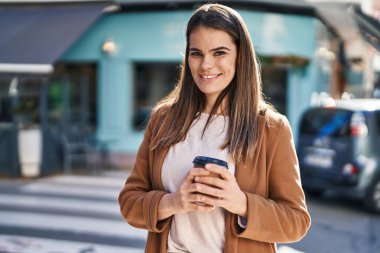 Young beautiful hispanic woman smiling confident drinking coffee at street