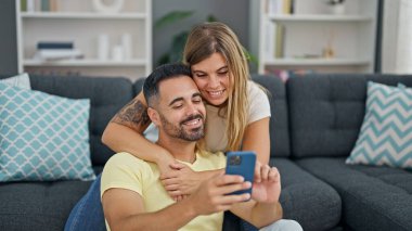 Man and woman couple using smartphone sitting on sofa at home