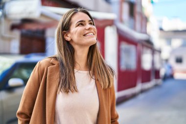Young beautiful hispanic woman smiling confident looking to the sky at street