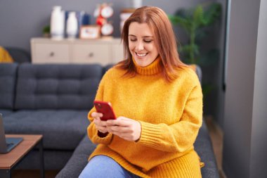 Young beautiful plus size woman using smartphone sitting on sofa at home
