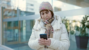 Ciddi bir ifadeyle caddede akıllı telefon kullanan olgun İspanyol kadın.