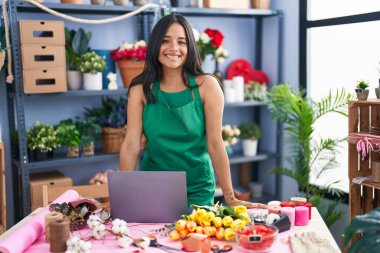 Young hispanic woman florist smiling confident using laptop at florist shop
