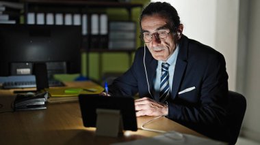 Ofiste çalışan orta yaşlı bir işçi dokunmatik ped ve kulaklık kullanıyor.