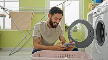 Çamaşır odasında gülümseyen, video oyunu oynayan İspanyol asıllı genç adam.