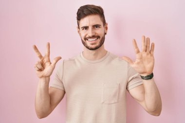 Sakallı İspanyol bir adam pembe arka planda duruyor. Sekiz numaralı parmaklarıyla işaret ediyor ve gülümsüyor. Kendinden emin ve mutlu.. 