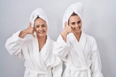 Beyaz bornoz ve havlu giymiş orta yaşlı bir kadın ve kızı telefonla konuşurken gülümsüyor. iletişim kavramları. 