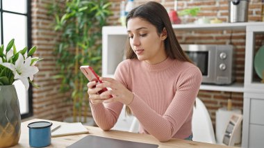 Genç, güzel, İspanyol bir kadın yemek masasında akıllı telefon kullanıyor.