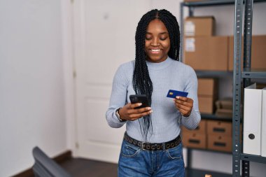 Afrika kökenli Amerikalı kadın ekommerans işçisi. Ofiste akıllı telefon ve kredi kartı kullanıyor.