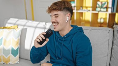 Genç İspanyol adam kanepede oturup evde şarkı söylüyor.