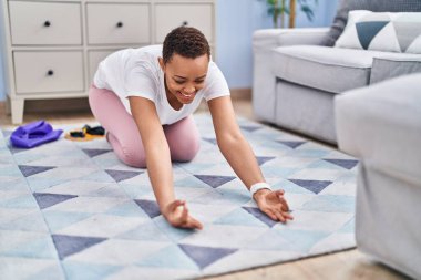 Afro-Amerikalı kadın gülümseyerek evde yoga eğitimi alıyor.
