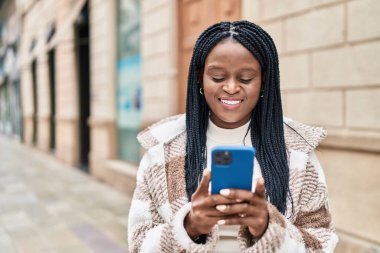 Afro-Amerikalı kadın sokakta akıllı telefon kullanarak kendine güveniyor.