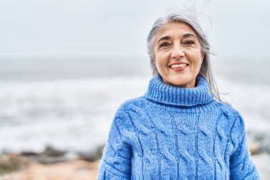 Orta yaşlı, kır saçlı, gülümseyen, kendine güvenen bir kadın.
