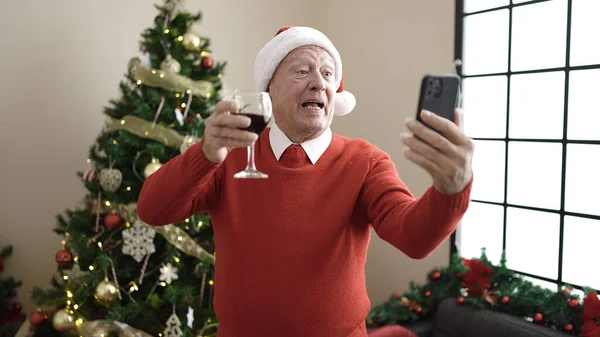 senior drinking wine doing video call at home
