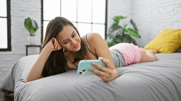 喜怒无常的年轻女子穿着睡衣躺在床上 在公寓舒适的卧室里打着一个愉快的视频电话 — 图库照片