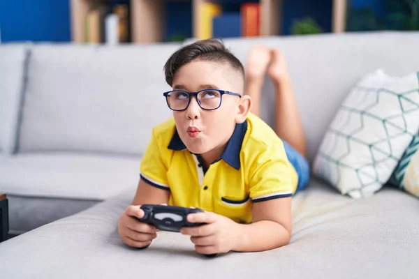 年轻的孩子在沙发上玩电子游戏 手里拿着控制器 用嘴和眼睛做鱼脸 疯狂而滑稽 — 图库照片