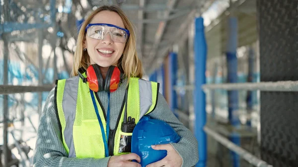 Young blonde woman builder smiling confident holding hardhat at street