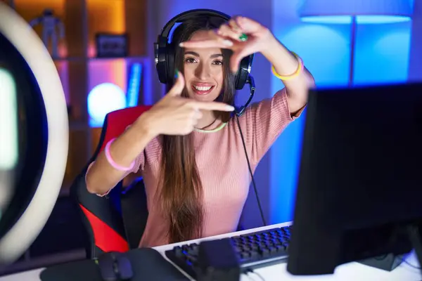 Young hispanic woman playing video games smiling making frame with hands and fingers with happy face. creativity and photography concept.