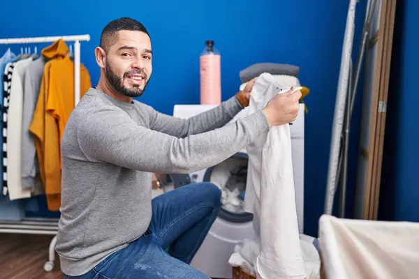 Young latin man smiling confident washing clothes at laundry room