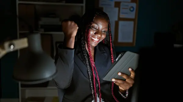 自信を持ったアフリカ系アメリカ人女性労働者がオフィスでタッチパッドでビジネスの成功を祝い 笑顔でボスのような勝者の美しい肖像画 夜になると 光の下で — ストック写真