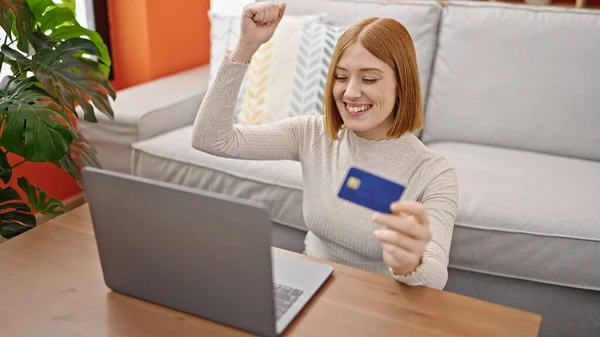 Young blonde woman shopping with laptop and credit card sitting on floor at home