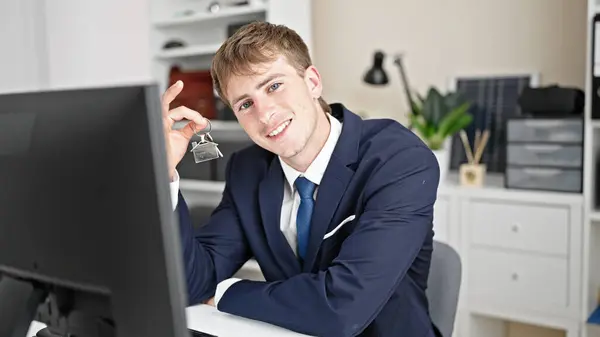 Young caucasian man real state agent holding keys of new home at office