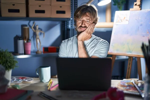 中年男子坐在艺术演播室里 晚上拿着笔记本电脑 满脑子疲惫 两臂交叉 对抑郁症感到厌烦 — 图库照片