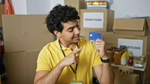 Young latin man volunteer pointing to credit card smiling at charity center