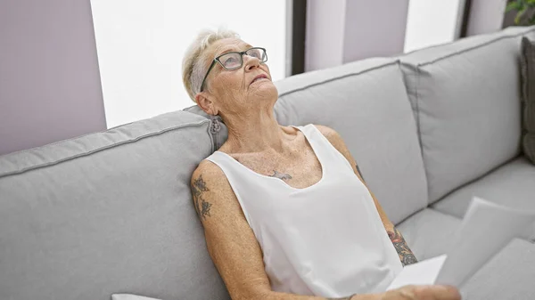 Mulher Cabelos Grisalhos Sênior Encontra Conforto Relaxamento Sofá Aconchegante Segurando — Fotografia de Stock