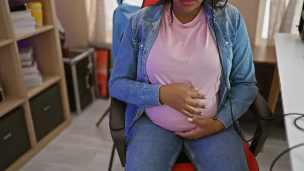 Expecting a baby! young pregnant gaming streamer touching belly, enjoying a late night virtual stream in her home gaming room