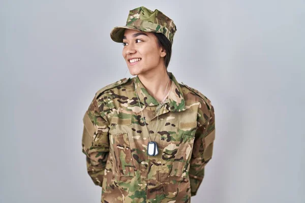 Young south asian woman wearing camouflage army uniform looking away to side with smile on face, natural expression. laughing confident.
