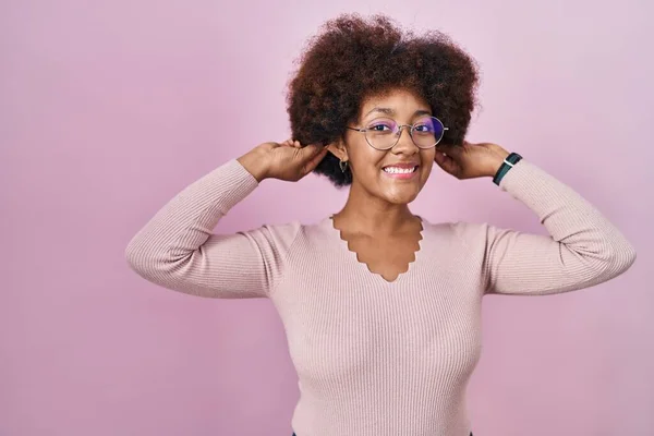 ピンクの背景の上に立っている若いアフリカ系アメリカ人女性は 指で耳を引く笑顔 面白いジェスチャー オーディション問題 — ストック写真