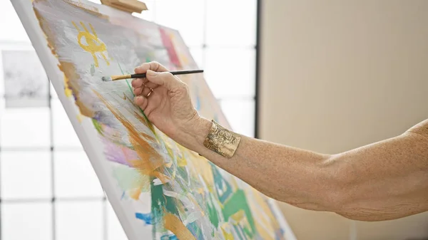 Senior woman artist\'s hands gracefully drawing on canvas in art studio, a lesson in creativity for mature students at the local academy