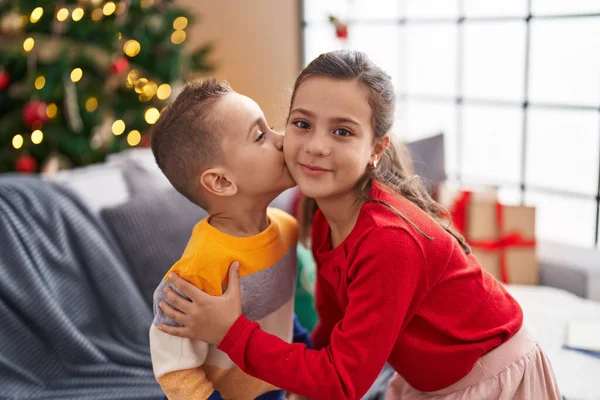 Brother and sister kissing and hugging each other standing by christmas tree at home