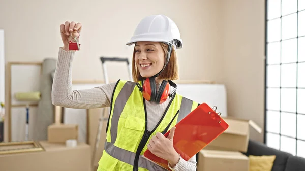 Young blonde woman architect holding keys of new home and clipboard at new home